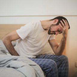 Man with a headache sits on the edge of his bed.