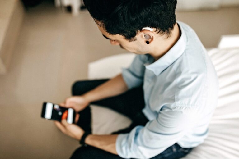 Younger man with a hearing aid using a smartphone.