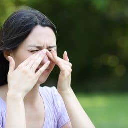 Woman experiencing sinus pressure in an outdoor environment.
