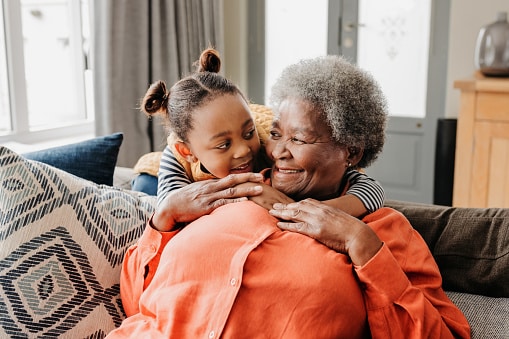 Happy grandmother and grandchild hugging on a couch at home.